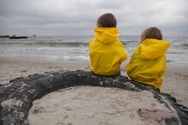          Dos niños con ropa amarilla se sientan en la playa y miran a un lado
. - Foto, imagen