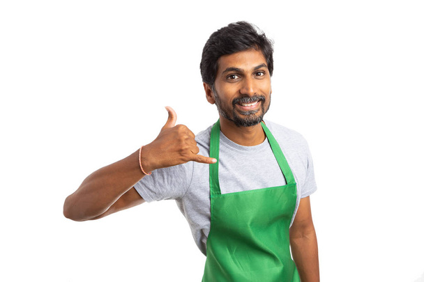 Дружественный супермаркет или гипермаркет индийский работник мужчина держа сотовый телефон жест на ухо с указательным и мизинец пальцы, как контакт с нами концепции изолированы на белом фоне студии
 - Фото, изображение