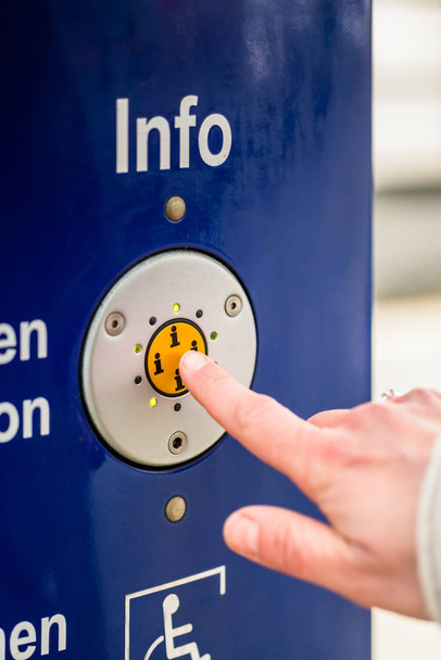 Женщина нажимает кнопку информации машины помощи на вокзале
 - Фото, изображение