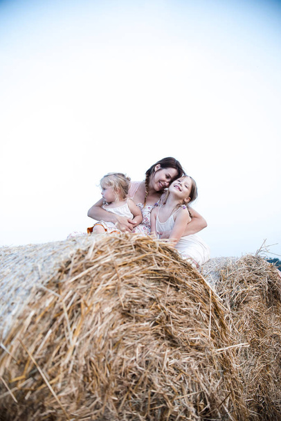 Young pregnant woman with two daughters having fun on hay in field - Фото, изображение