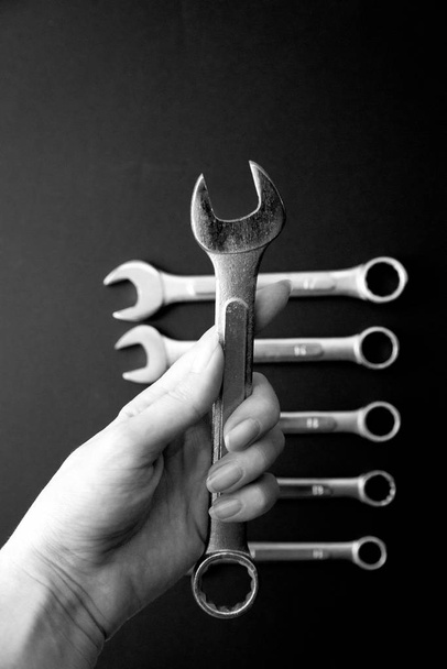 Meninas mão segurando chave inglesa, chaves em um fundo preto. Ferramentas para reparação.Preto e branco, monocromático
. - Foto, Imagem