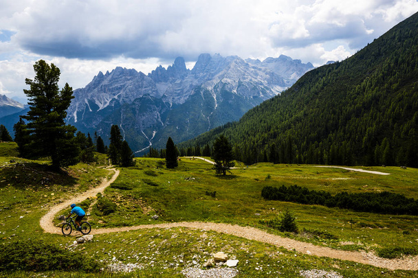 Tourist cycling in Cortina d'Ampezzo, stunning rocky mountains on the background. Man riding MTB enduro flow trail. South Tyrol province of Italy, Dolomites. - Photo, Image