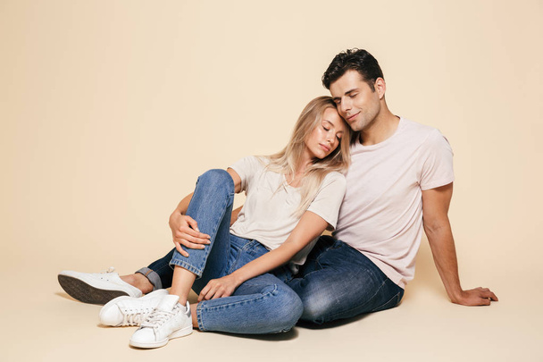 Portrait of a happy young couple sitting together over beige background, hugging - Fotó, kép