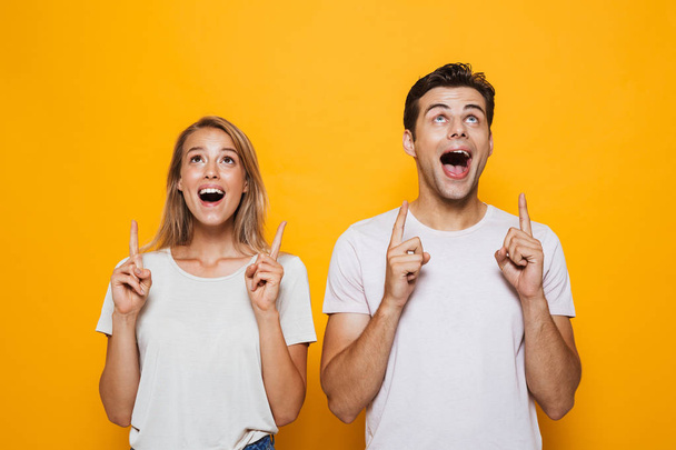 Photo of happy excited young loving couple standing isolated over yellow wall background pointing. - Foto, immagini