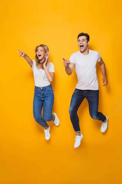 Full length portrait of happy young couple pointing fingers away isolated over background, jumping - Photo, Image