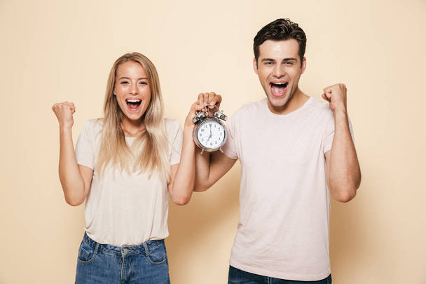 Image of happy young loving couple holding alarm clock isolated make winner gesture. - Foto, immagini