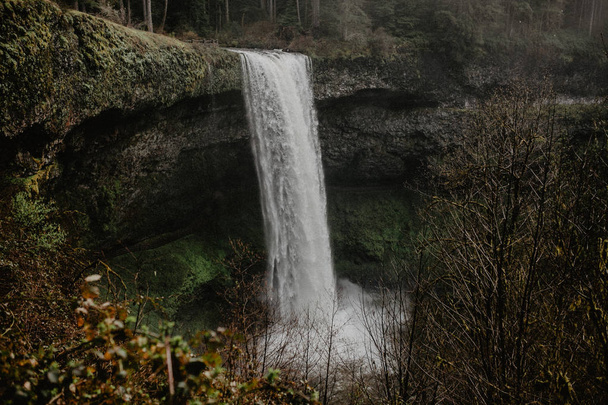  waterfall over rock cliff of cascading water splashing into river - Fotoğraf, Görsel