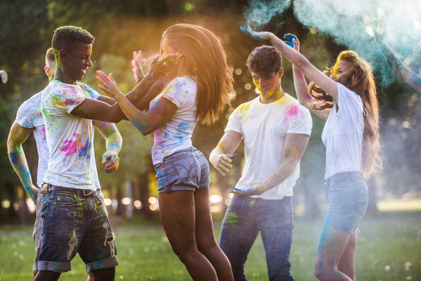 Group of happy friends playing with holi colors in a park - Young adults having fun at a holi festival, concepts about fun, fun and young generation - Foto, imagen