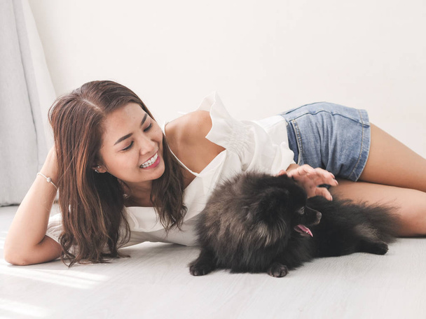 Happy Asian woman lying on floor and touching her black dog, lifestyle concept. - Фото, изображение