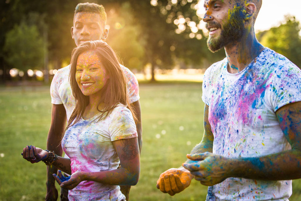 Grupo de amigos felices jugando con colores holi en un parque - Adultos jóvenes divirtiéndose en un festival holi, conceptos sobre diversión, diversión y generación joven
 - Foto, Imagen