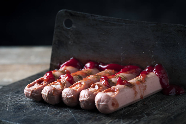 close-up de alguns cachorros-quentes assustadores na forma de dedos sangrentos cortados com um cutelo, em uma tábua de corte rústico
 - Foto, Imagem