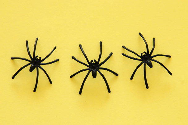 Halloween holiday concept. Black spiders over yellow background. Top view, flat lay - Фото, изображение