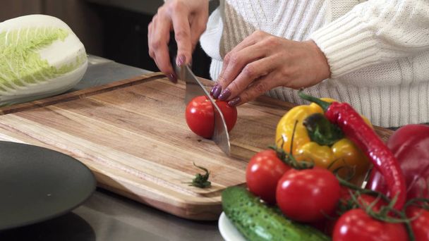 Close up cropped shot of a woman slicing tomato on a wooden cutting board - Foto, Bild