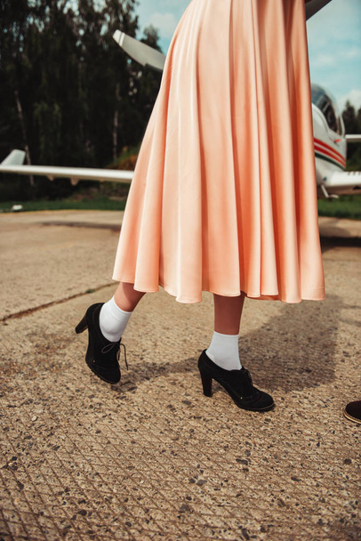 cropped view of female legs in romantic evening dress and shoes standing near plane   - Foto, immagini