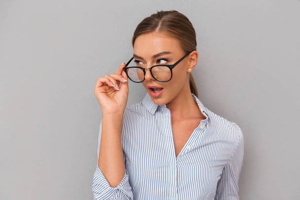 Image of beautiful shocked business woman standing over grey wall background wearing glasses. - 写真・画像