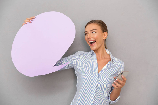 Image of beautiful business woman standing over grey wall background with speech bubble chatting by mobile phone. - Фото, зображення