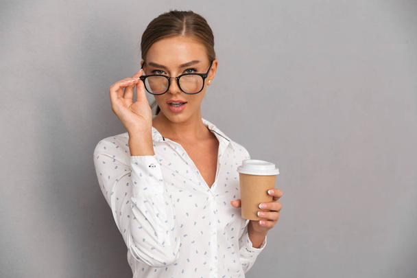 Image of beautiful business woman standing over grey wall background drinking coffee wearing glasses. - Фото, изображение