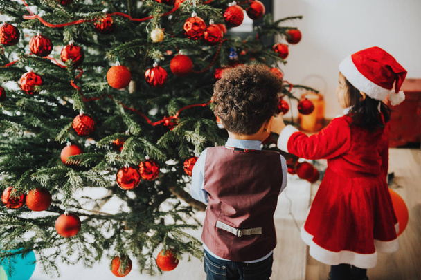 Groep van twee kleine kinderen spelen met kerstboom thuis - Foto, afbeelding