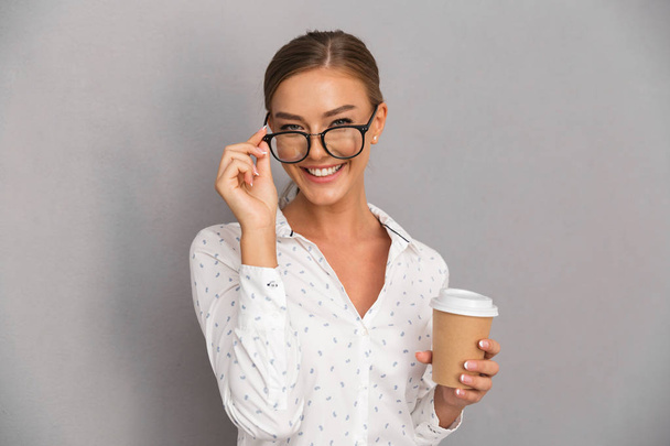Image of beautiful business woman standing over grey wall background drinking coffee wearing glasses. - Foto, Bild