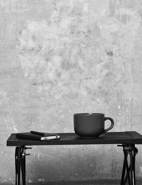 red tea or coffee cup or ceramic mug for drink copybook and pen black tray on beige textured background, copy space. - 写真・画像