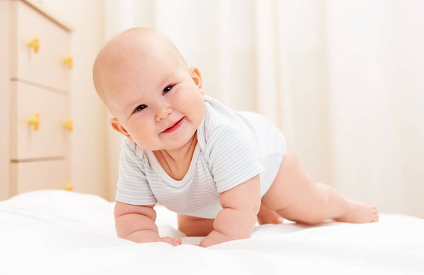 Happy smiling child crawling on the bed at home. Baby care concept. - Fotó, kép
