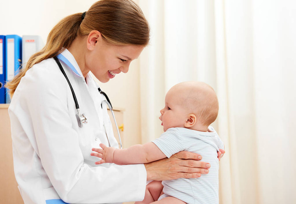 Cheerful female pediatrician holding cute child during general examination. Baby care. - Photo, image