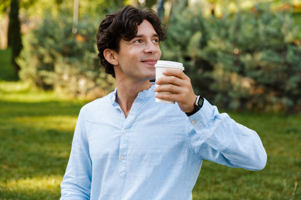 Csinos, fiatal alkalmi férfi kávét iszik a Városliget járás közben - Fotó, kép