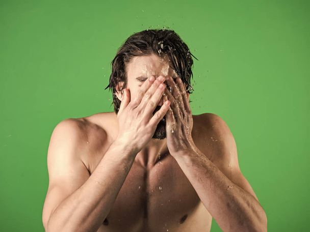 Man splash water at face on green background. - Zdjęcie, obraz