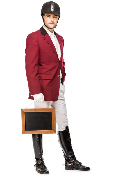 attractive young horseman in uniform holding blank chalkboard and looking at camera isolated on white - Foto, Bild