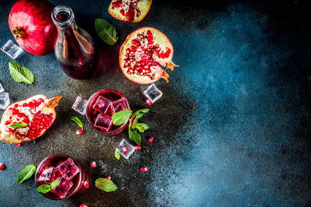 Fall cold beverage ideas, pomegranate cocktail, sparkling water with mint and ice cubes, dark blue background copy space top view - Photo, Image