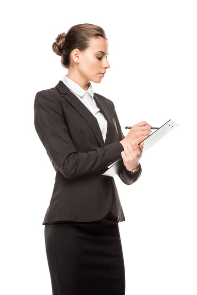 side view of beautiful young businesswoman writing in clipboard isolated on white - Foto, imagen