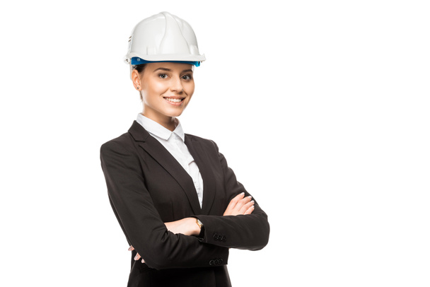 красивая молодая архитектор в шлеме и костюме смотрит в камеру со скрещенными руками, изолированными на белом
 - Фото, изображение