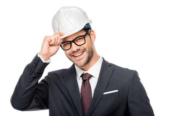 portrait of laughing young male architect adjusting hard hat isolated on white  - Foto, imagen