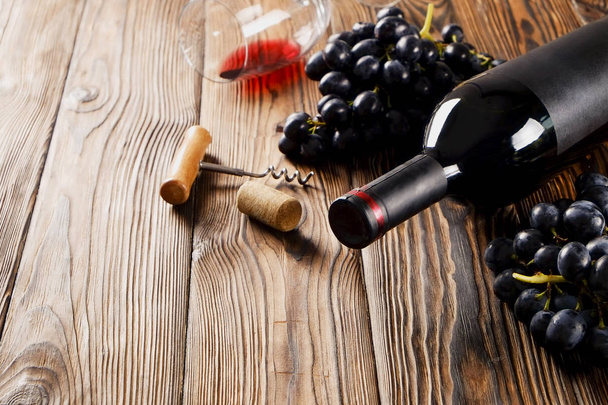 Vintage bottle of red wine with blank matte black label, corkscrew & bunches grapes on wooden table background. Expensive bottle of cabernet sauvignon concept. Copy space, top view, flat lay. - Photo, image
