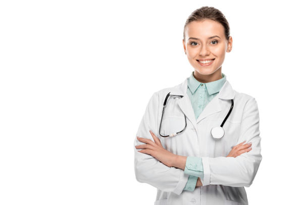 felice bella donna medico in cappotto medico in piedi con le braccia incrociate isolato su bianco  - Foto, immagini