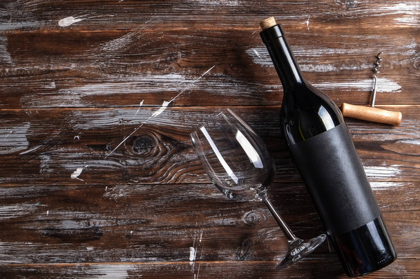 Vintage bottle of red wine with blank matte black label, corkscrew on grunged wooden table background. Expensive bottle of cabernet sauvignon concept. Copy space, top view, flat lay. - Foto, afbeelding