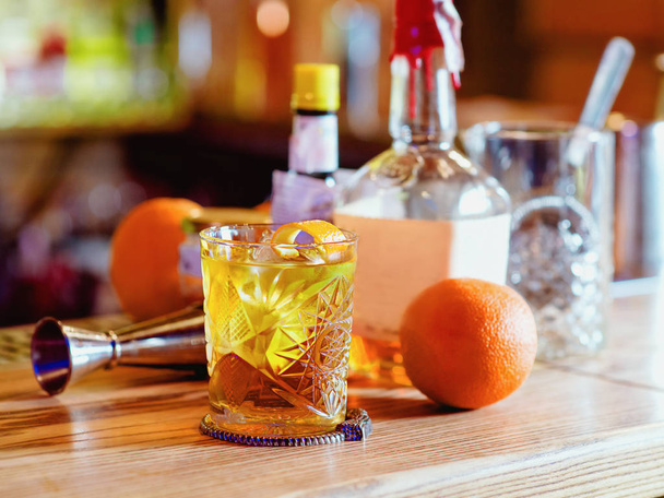 Старомодный коктейль, апельсин, бутылки и стакан на барной стойке
 - Фото, изображение