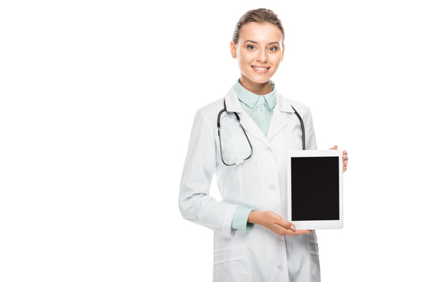 smiling female doctor in medical coat showing digital tablet with blank screen isolated on white - 写真・画像