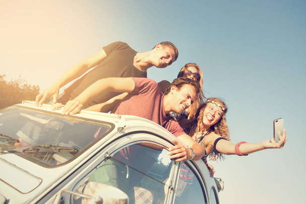 Groupe de personnes heureuses prenant un selfie dans une voiture au coucher du soleil en été
. - Photo, image