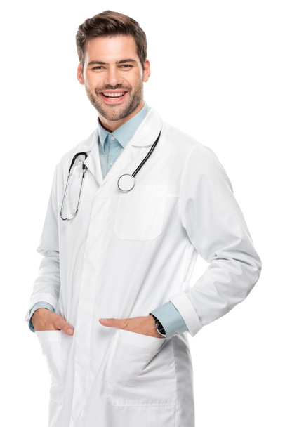 smiling young male doctor with stethoscope over neck in medical coat isolated on white  - Foto, immagini