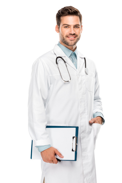 cheerful young male doctor with stethoscope over neck holding clipboard isolated on white - Φωτογραφία, εικόνα