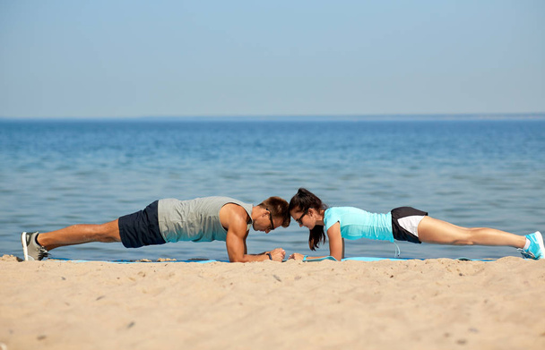 couple doing plank exercise on summer beach - Foto, afbeelding