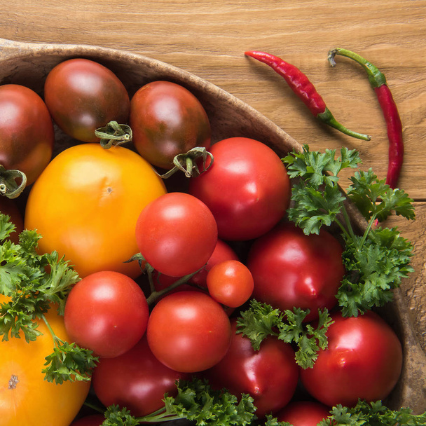 Square close up of fresh colorful organic tomatoes, green parsley and red peppers. Flat lay on natural wooden table surface. Selective focus. Healthy eating and dieting concepts. - Foto, imagen