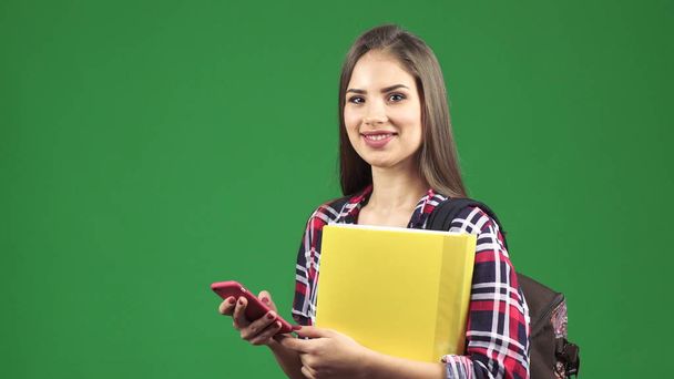 Houkutteleva nuori naispuolinen opiskelija käyttää älypuhelinta hymyillen kameralle
 - Valokuva, kuva