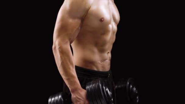 Homem flexiona as mãos com halteres, treinando seus bíceps em um fundo preto no estúdio
 - Filmagem, Vídeo