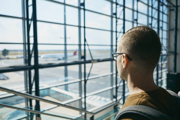 Young passenger waiting at airport and looking through window to airplane. - Photo, Image