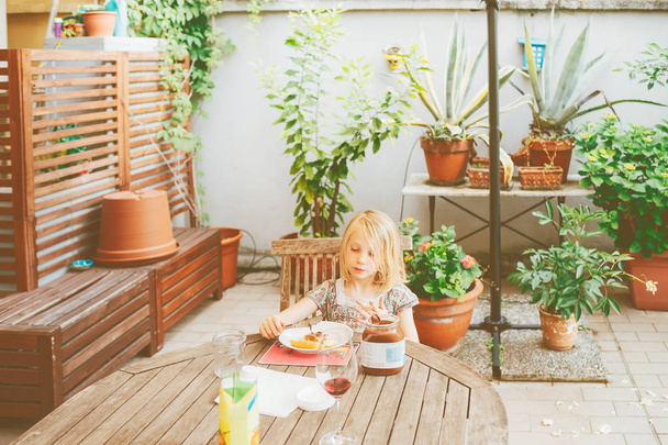 female child outdoor sitting table having breakfast - morning routine, eating, hunger concept - Photo, Image