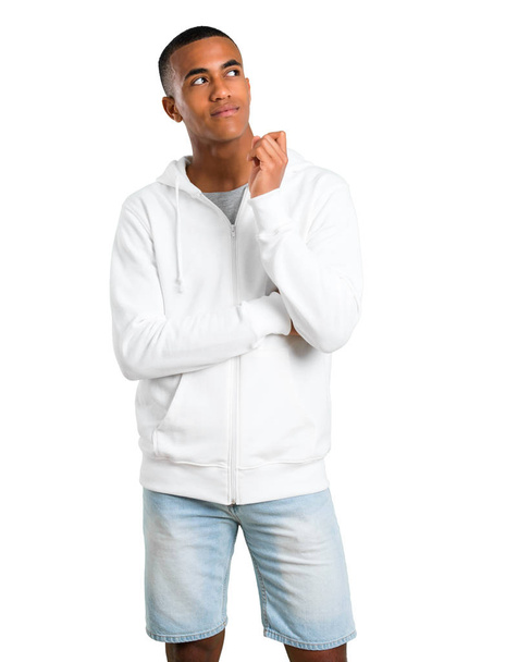 Dark-skinned young man with white sweatshirt pointing with the index finger a great idea and looking up on isolated white background - Photo, Image