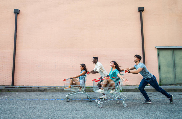 Gruppo multietnico di amici che giocano con i carrelli della spesa in un parcheggio
 - Foto, immagini