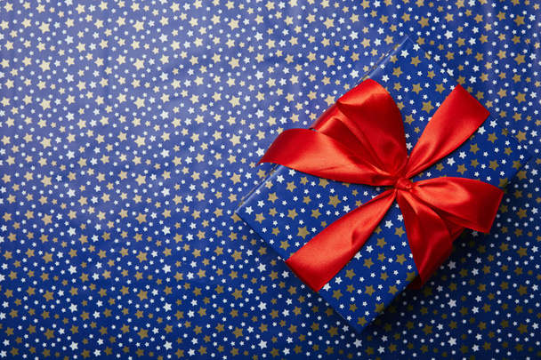 top view of wrapped gift box with red ribbon on festive wrapping paper with stars pattern - Photo, Image